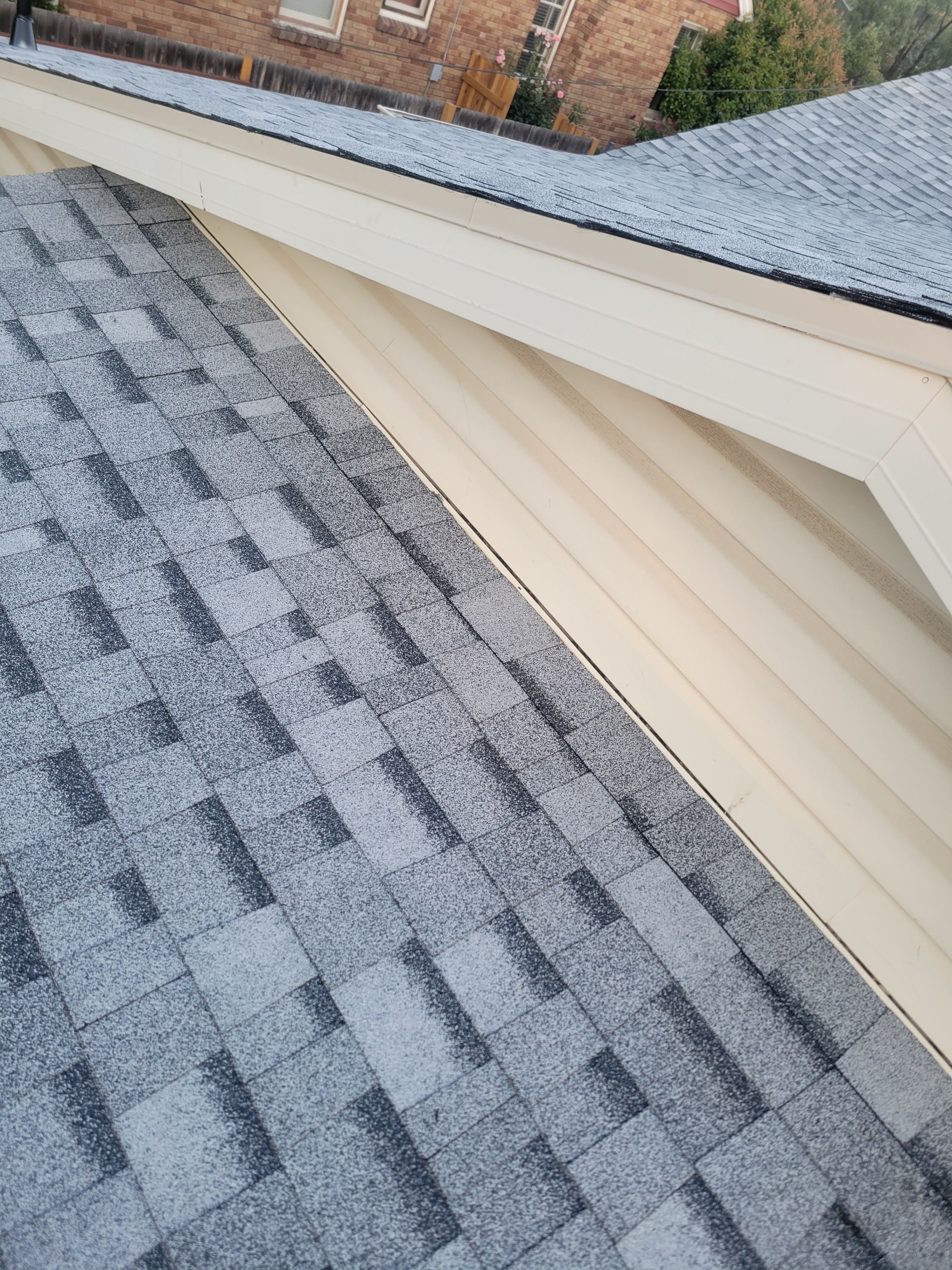 Snow-dusted gray shingle roof beside cream siding and a brick house wall