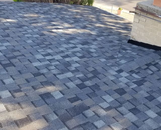 Blue-gray shingled roof with a chimney and sunlight patches