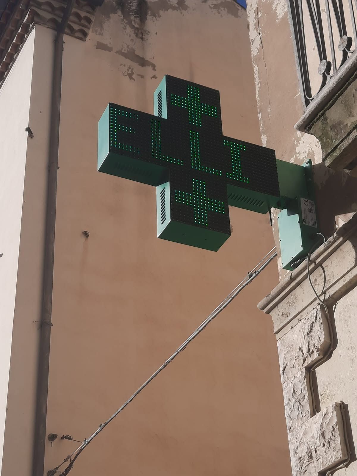 Insegna luminosa verde a forma di croce di una farmacia su un edificio in una strada stretta