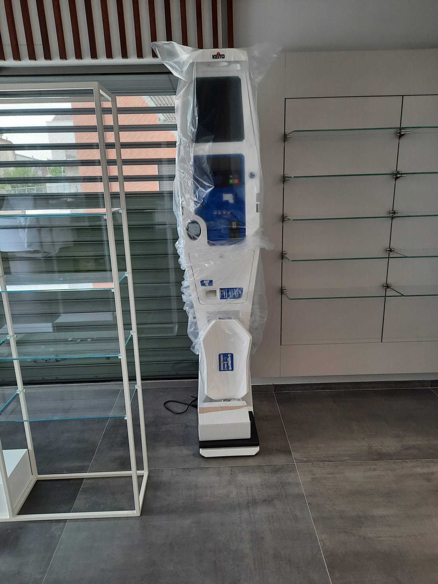 Chiosco bianco su un pavimento scuro accanto a scaffali metallici vuoti in un luminoso spazio commerciale o di magazzino.