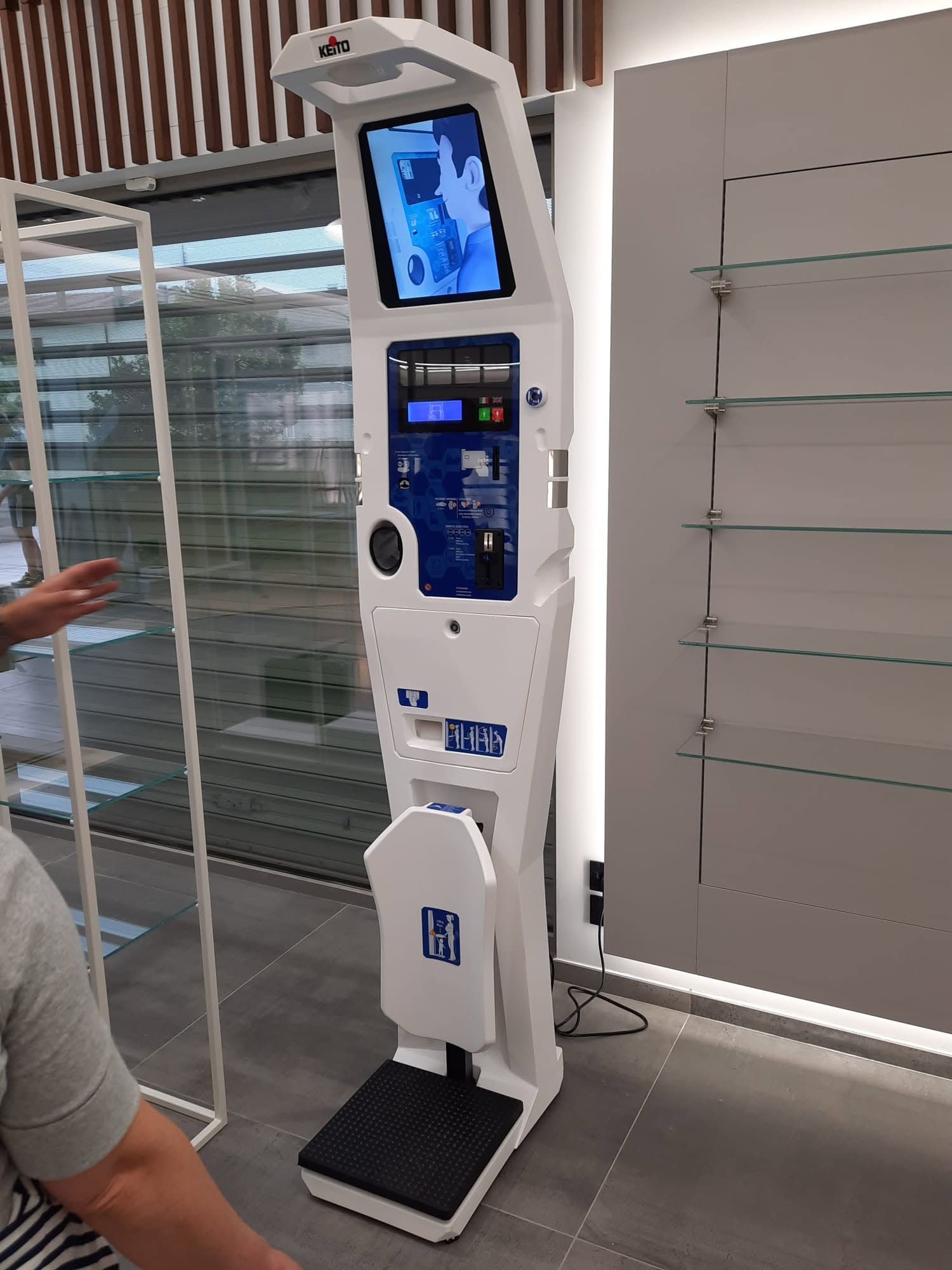 Chiosco self-service alto e bianco con schermo blu e poggiapiedi in una corsia di un negozio.