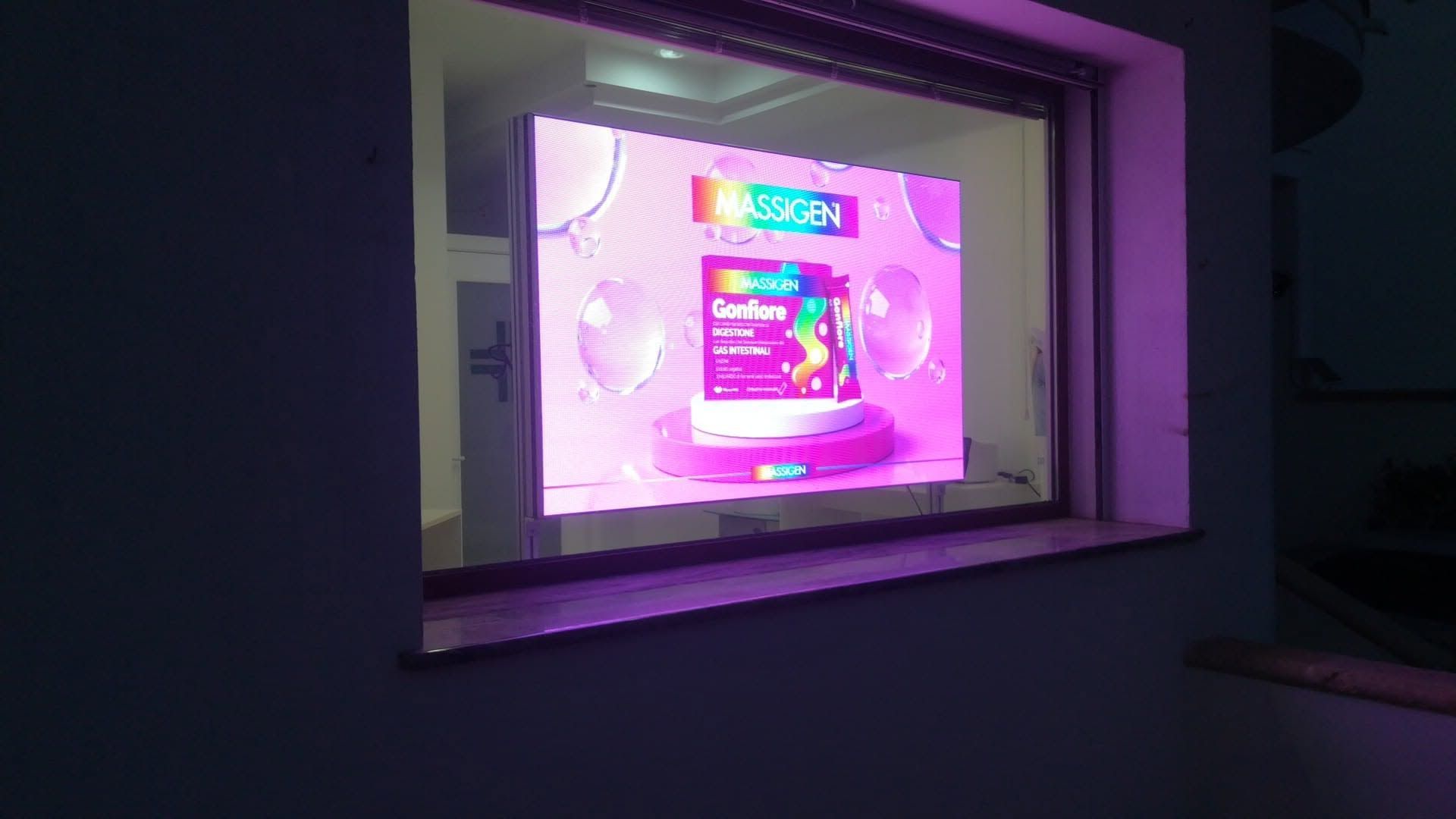 Una vetrina rosa brillante in una stanza buia, con la pubblicità di un prodotto dietro un vetro.