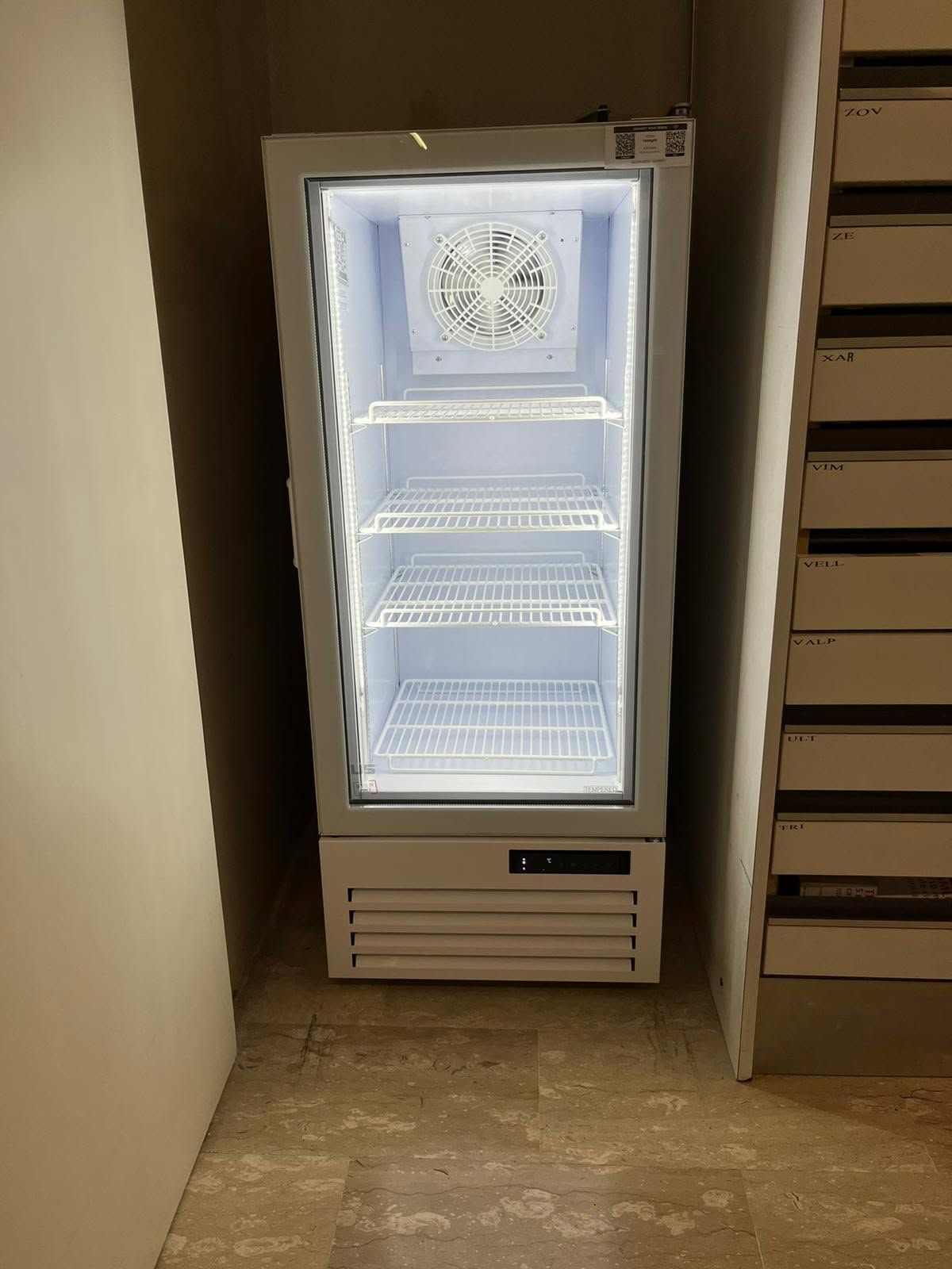 Frigorifero aperto con interno illuminato e ripiani vuoti in un corridoio o in una nicchia della cucina.