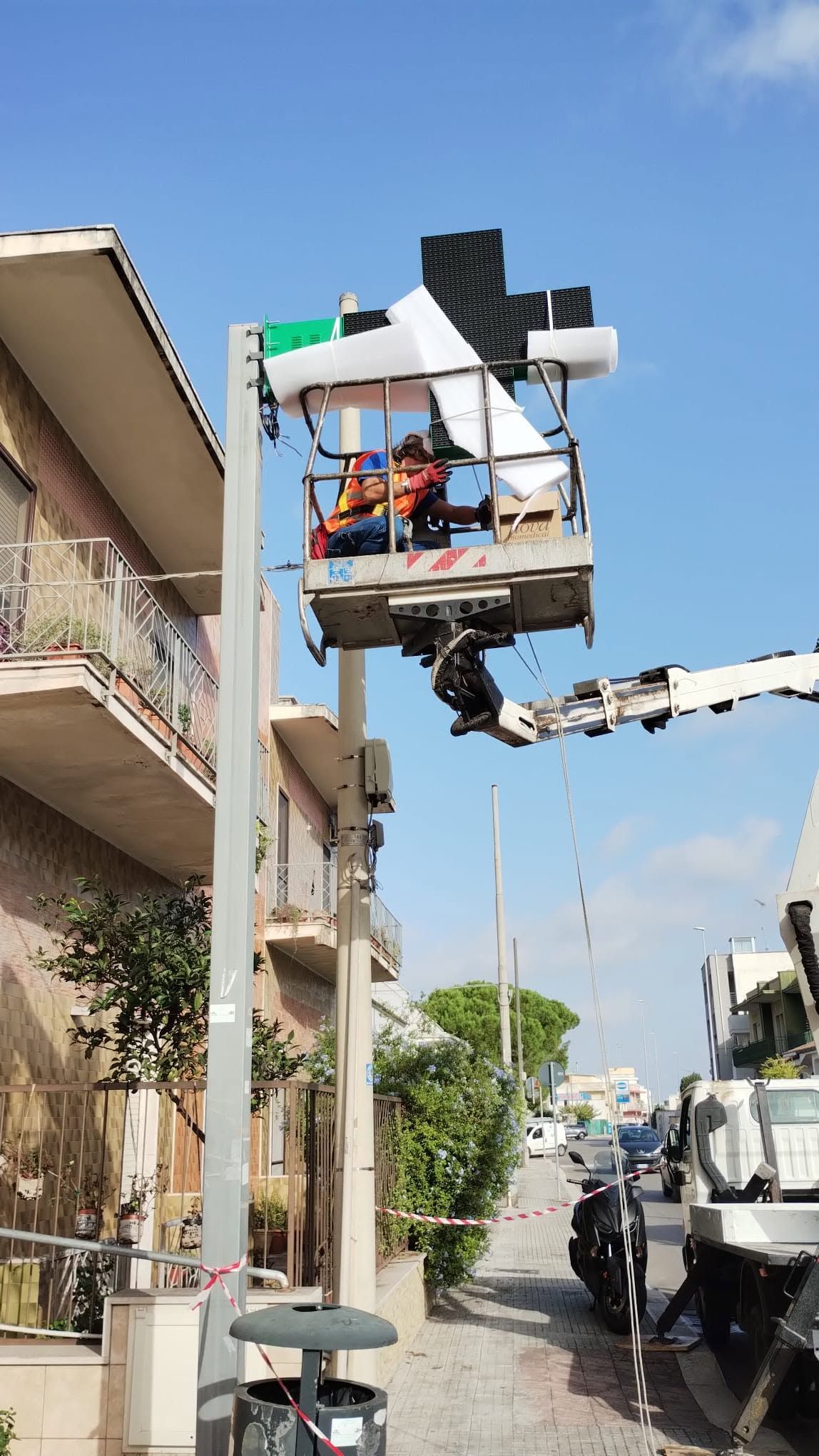 Un operaio di una società di servizi pubblici ripara le linee elettriche aeree su una piattaforma elevatrice in una strada residenziale.
