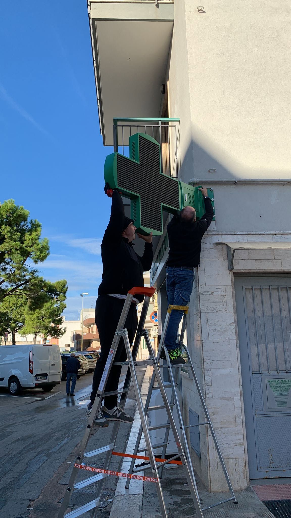 Due operai su una scala installano una tenda da sole verde sulla facciata di un edificio.
