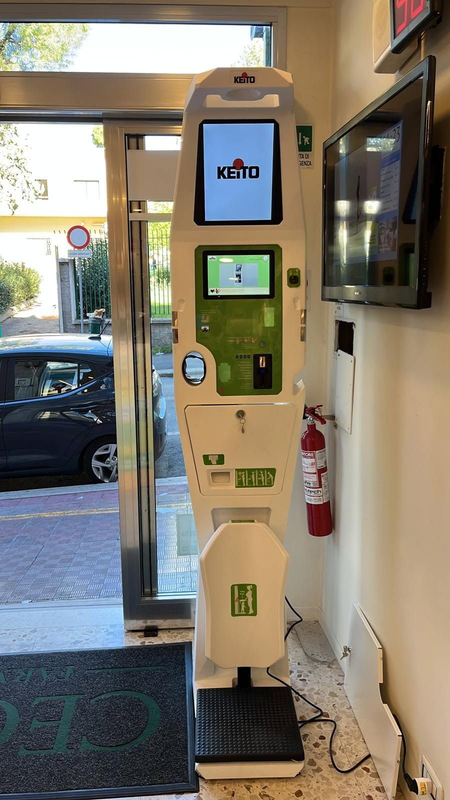 Chiosco bianco per il pagamento del parcheggio all'interno dell'ingresso di un edificio, con schermo tattile e lettore di carte vicino alla porta.