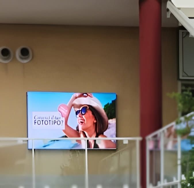 Cartellone pubblicitario con una donna sorridente con occhiali da sole e cappello che pubblicizza FOTO TIPI, dietro una ringhiera