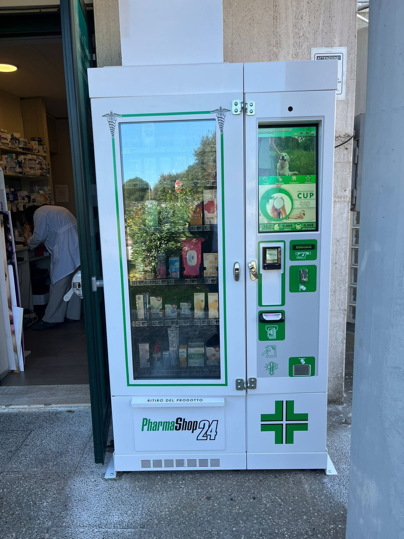 Distributore automatico bianco con frontale in vetro e dettagli verdi, posizionato all'esterno di un edificio.