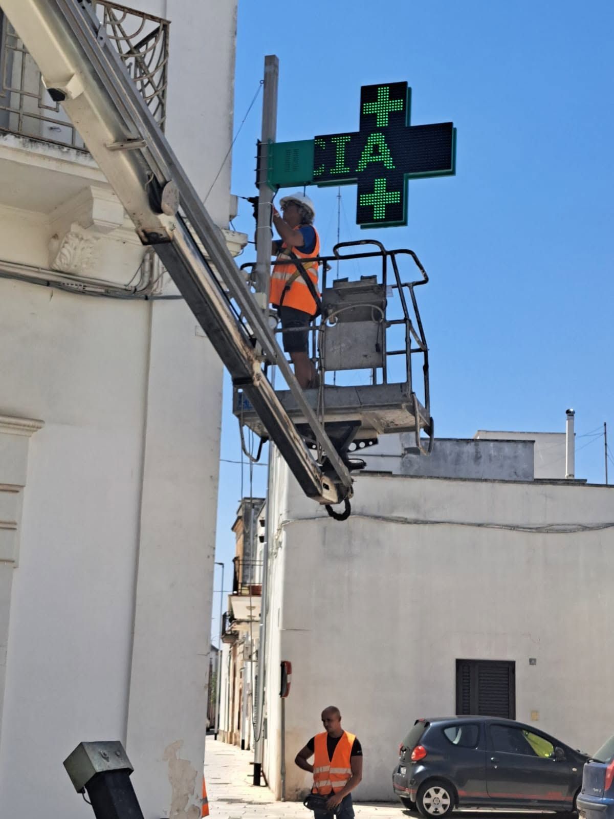 Operai con giubbotti arancioni riparano un semaforo verde sulla facciata di un edificio.