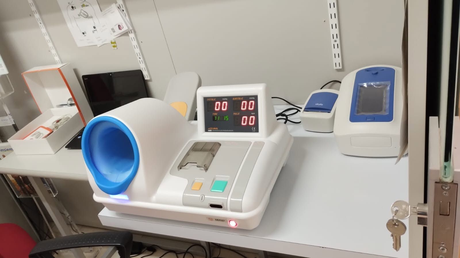 Banco da laboratorio con centrifuga blu, bilancia digitale e dispositivo medico su un piano bianco.
