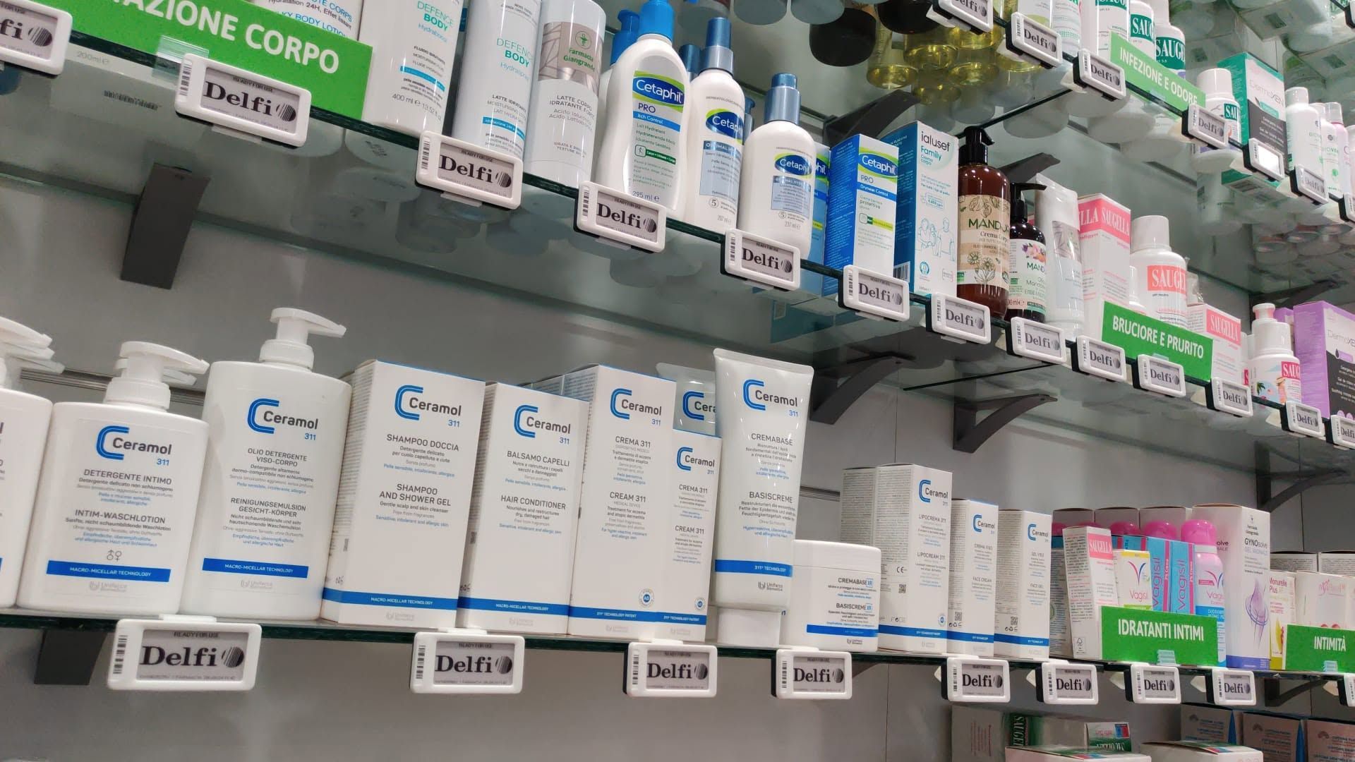 Lo scaffale della farmacia è rifornito di scatole e flaconi di medicinali di vario tipo, tra cui confezioni verdi e bianche.