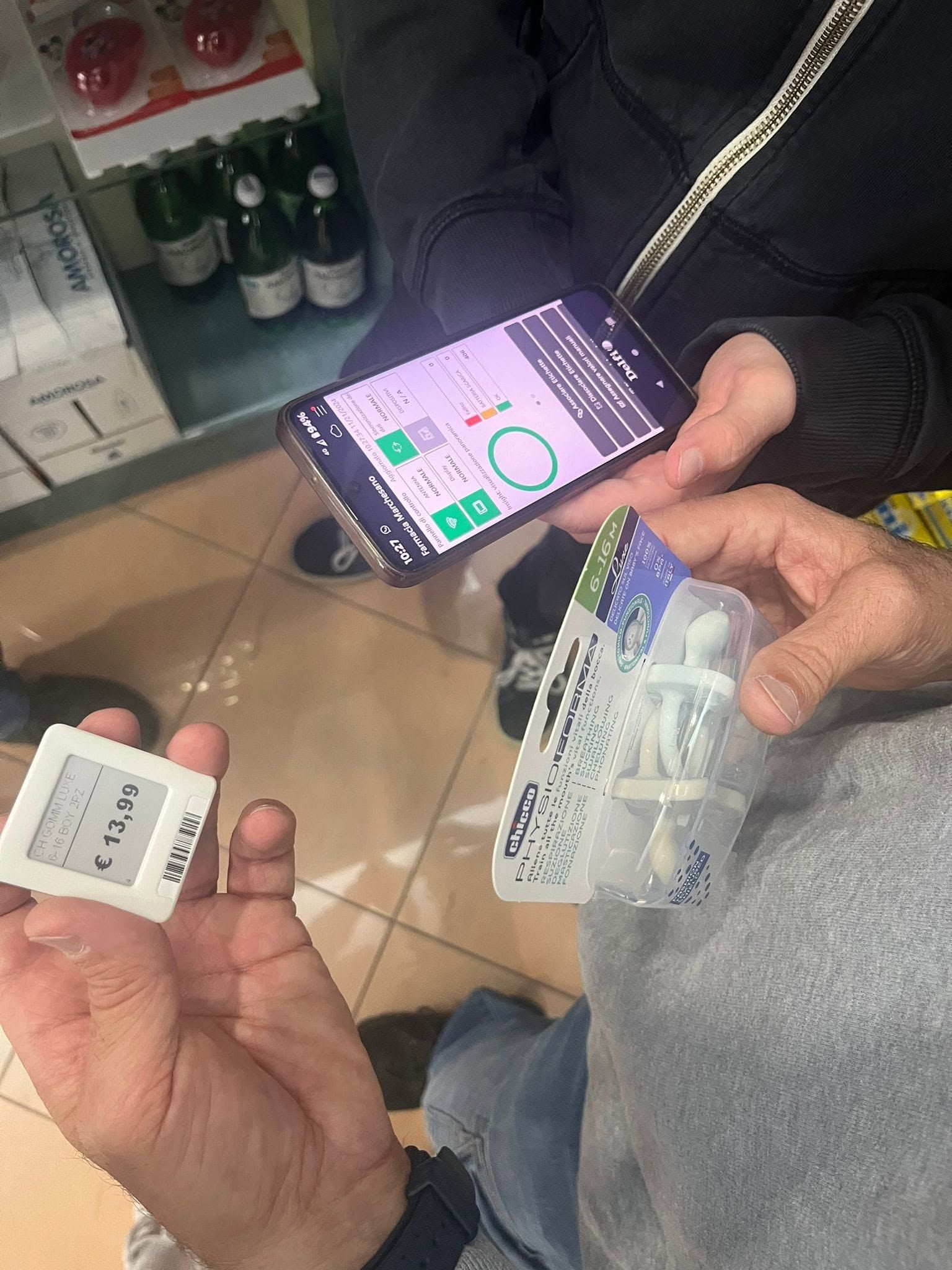 Mani che reggono un piccolo dispositivo e un telefono che mostra un'app di misurazione in una corsia di un negozio.