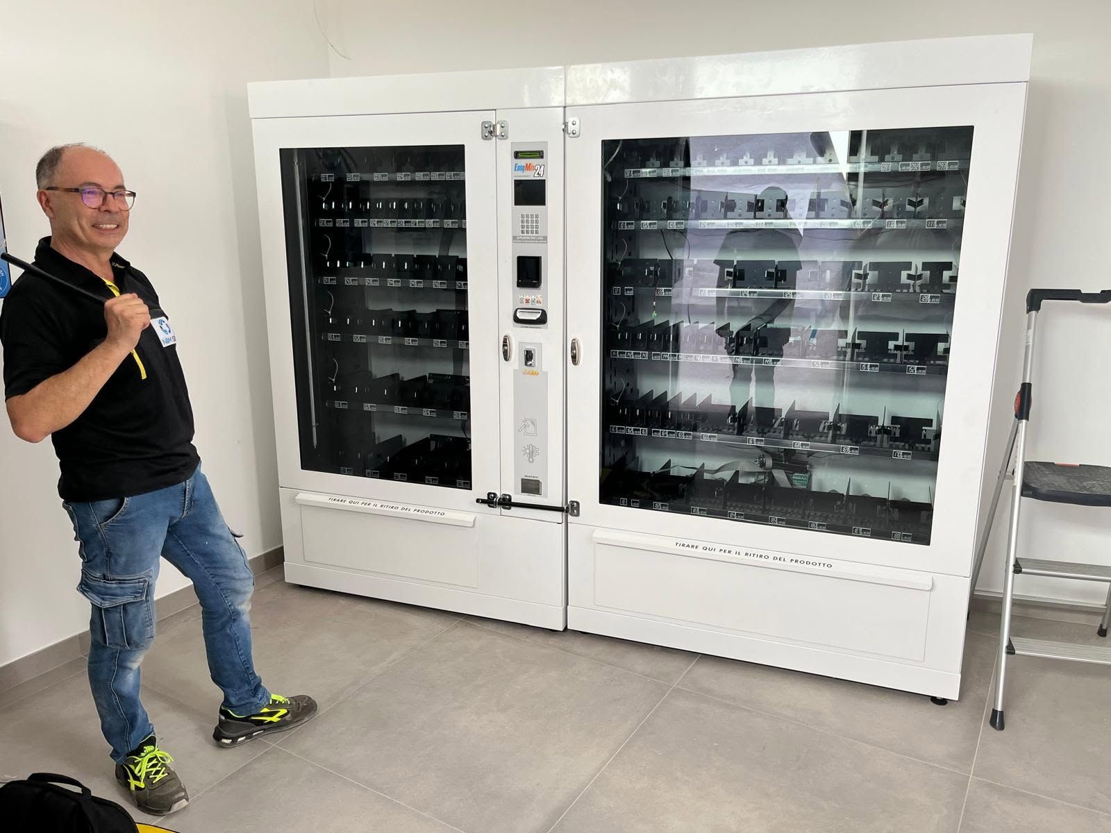 Un uomo in piedi accanto a un grande distributore automatico bianco in una stanza luminosa.