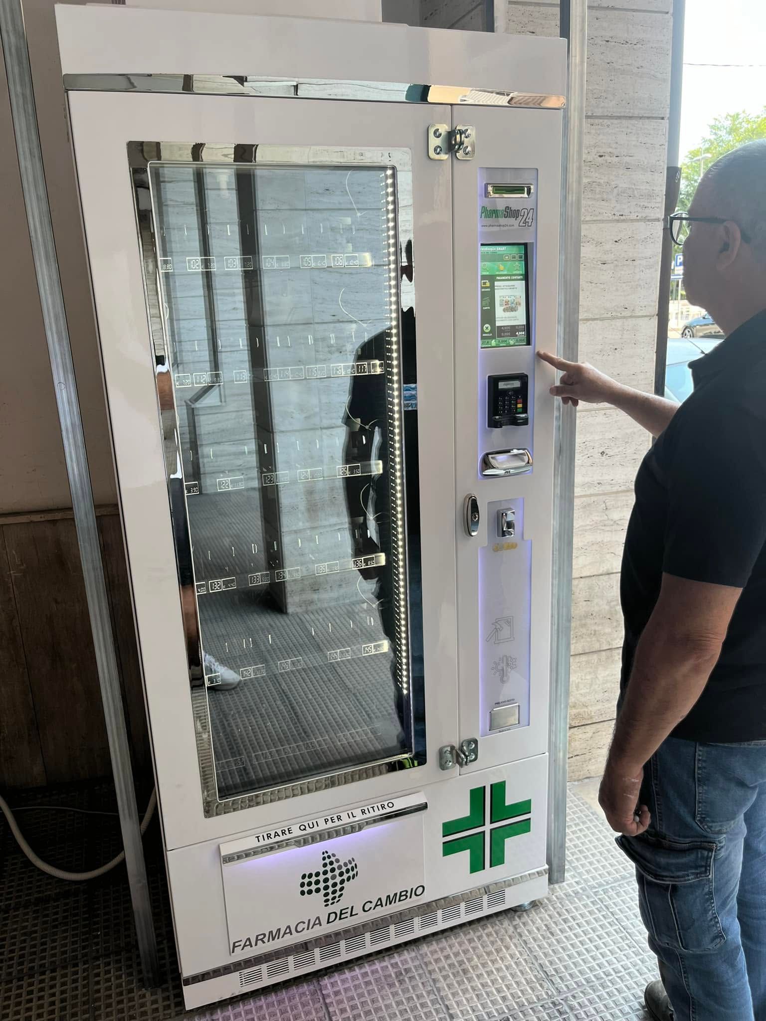 Persona che aziona un distributore automatico bianco con sportello in vetro in un luminoso corridoio interno.