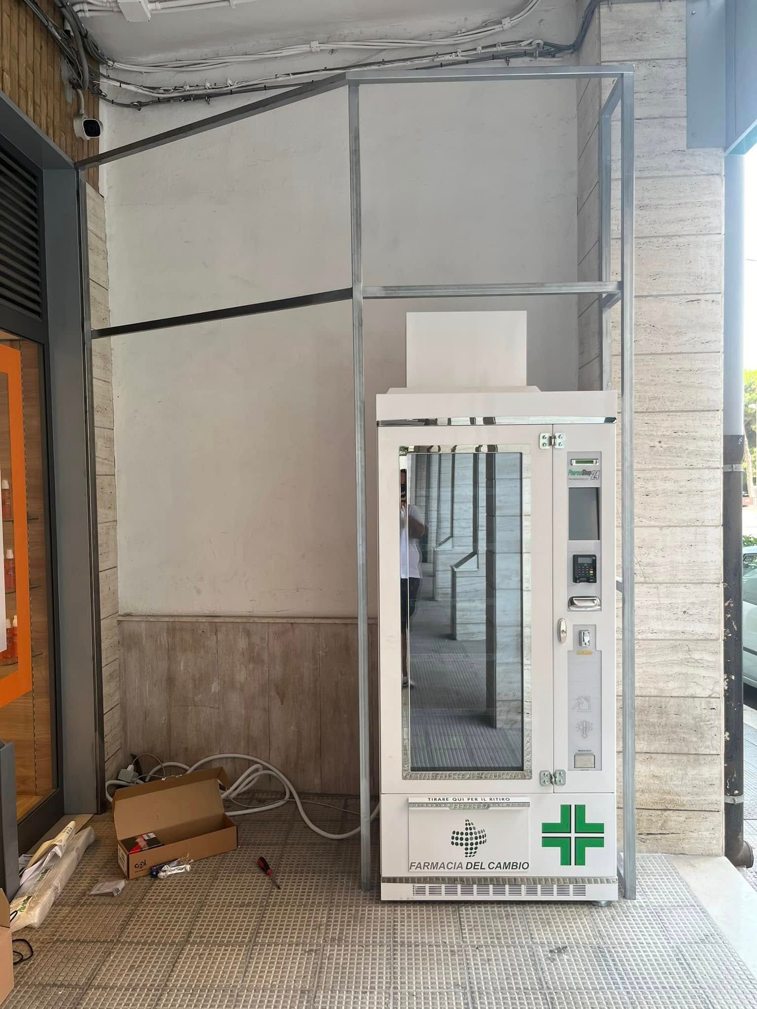 Cabina telefonica pubblica in un corridoio di cemento, bianca con una croce verde.