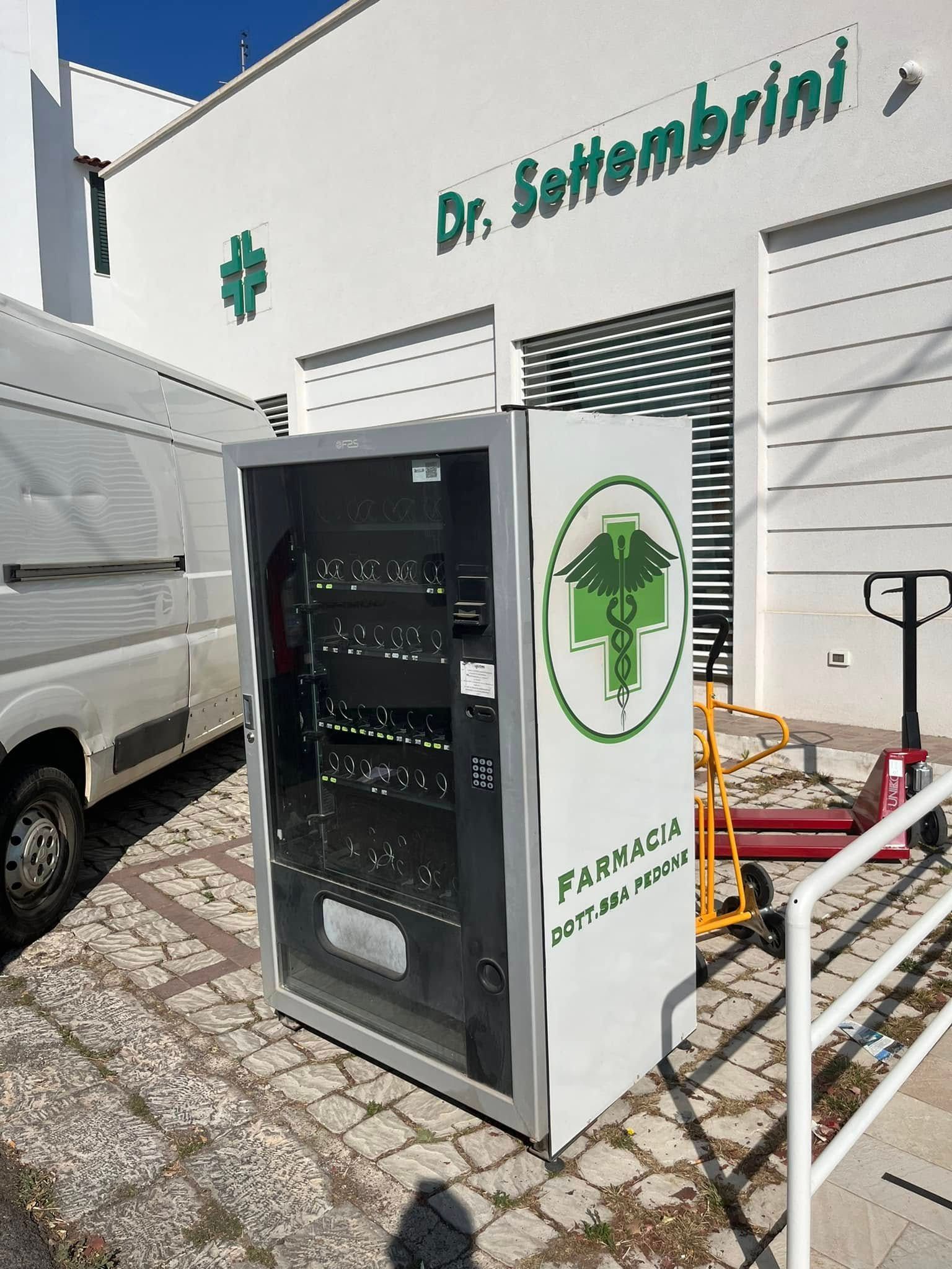 Armadio frigorifero medico verde per esterni, situato all'esterno della clinica del dottor Sobrinh, accanto a un furgone bianco con sportello in vetro aperto.