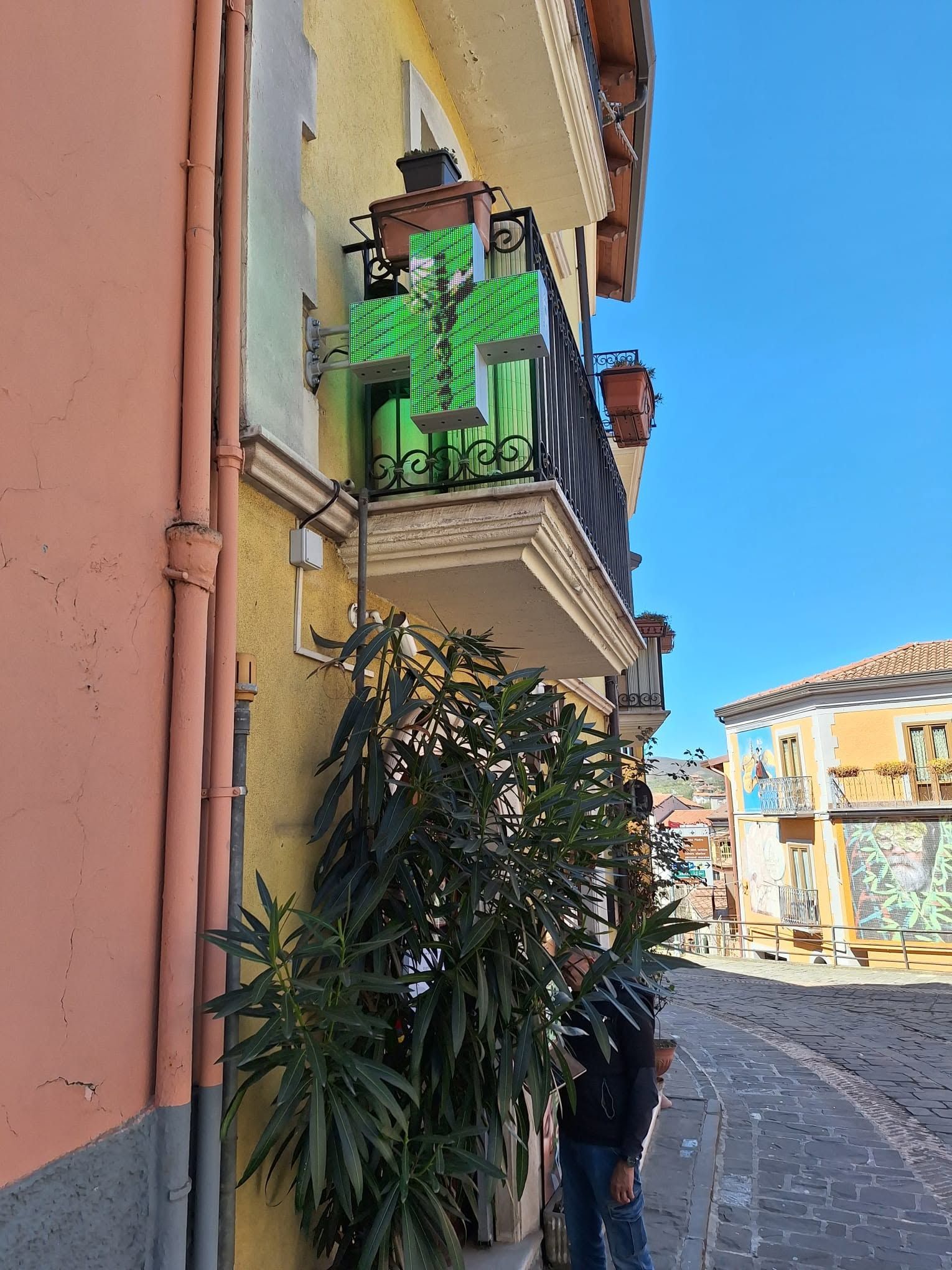 Stretta strada acciottolata con edifici color pastello, balconi verdi e piante in vaso in piena luce del sole
