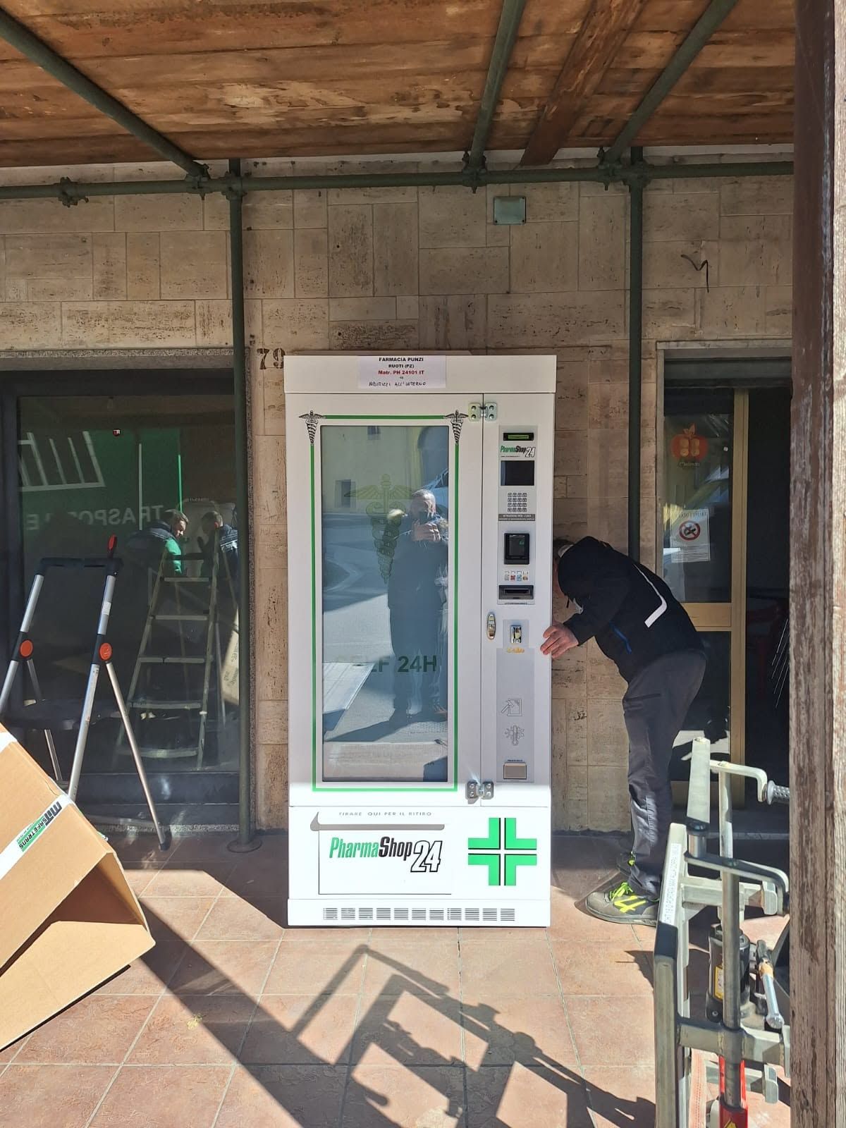 Chiosco automatico per il controllo della temperatura all'esterno di un edificio, con una persona china verso di esso.