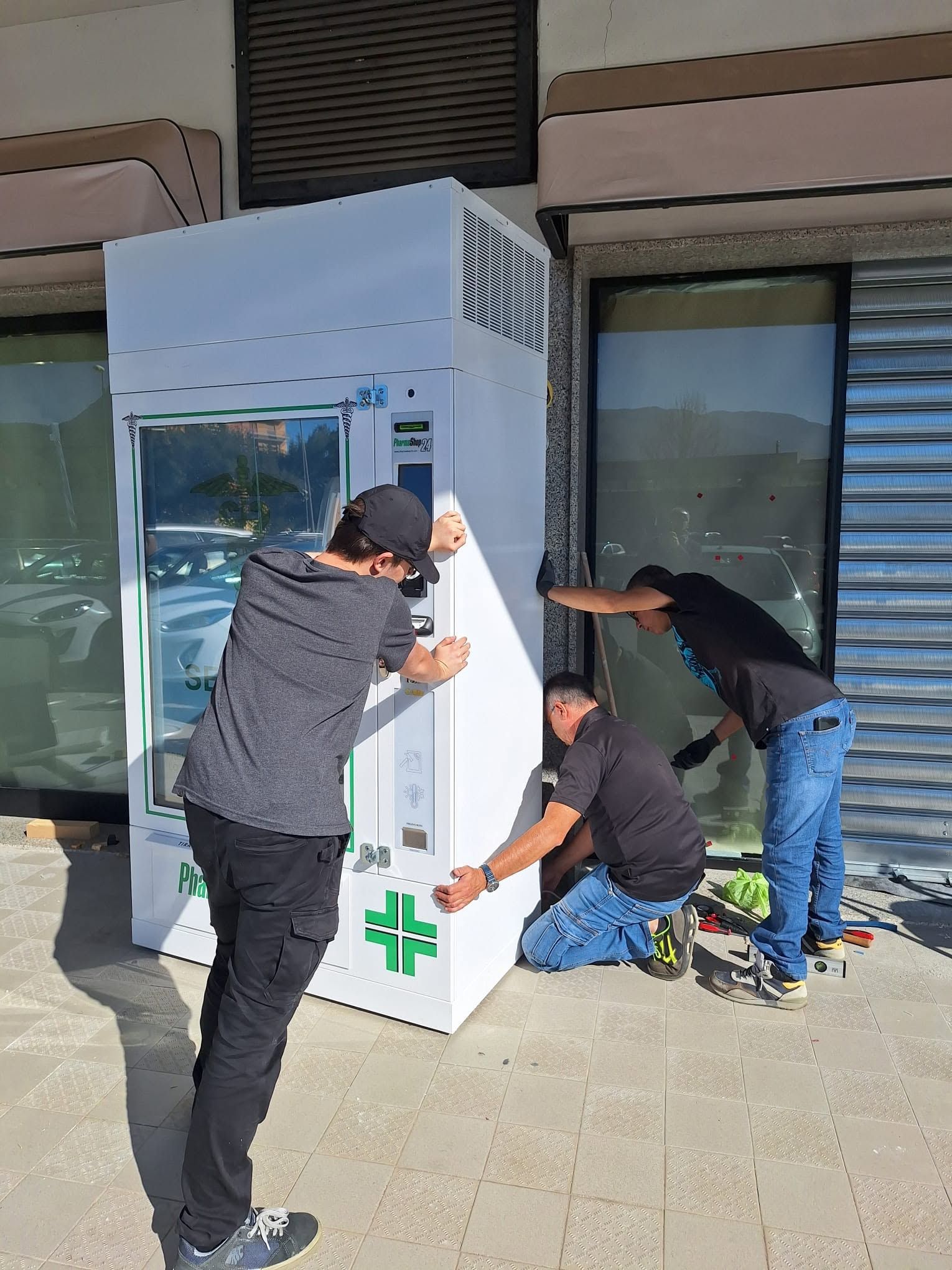 Tre operai installano un elettrodomestico bianco all'esterno di un negozio.