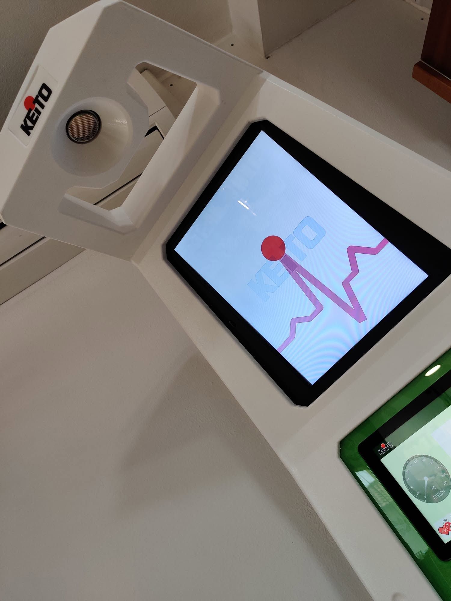 Schermo a parete per interni che mostra un grafico a linee rosa e un punto rosso, accanto a un dispositivo bianco e a un display verde.