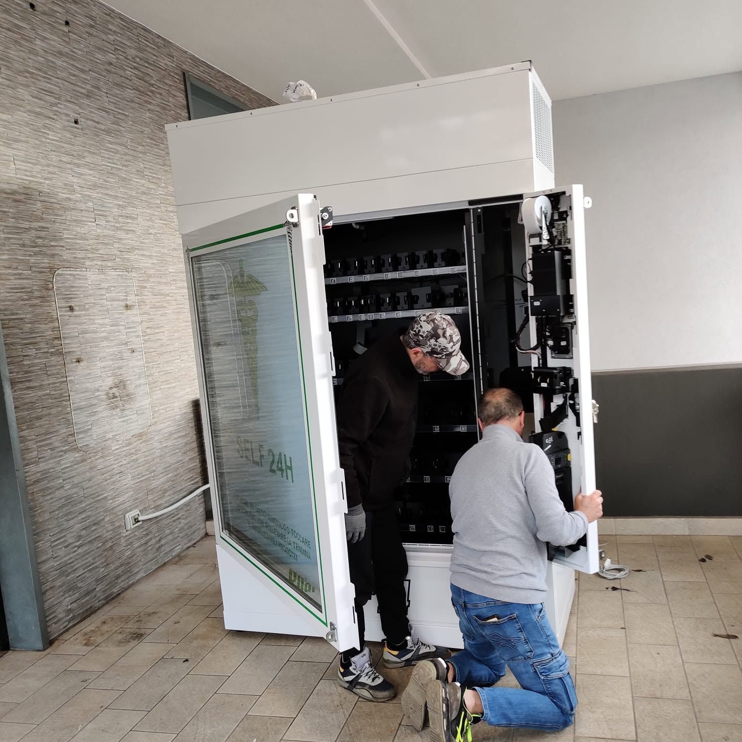 Due persone ispezionano un armadio server aperto in una stanza piastrellata.