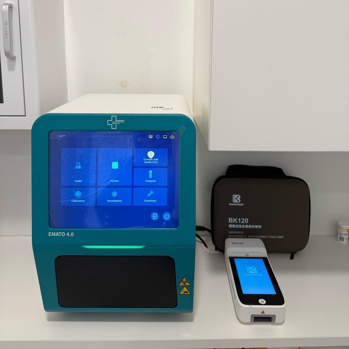 Uno strumento da laboratorio blu e verde acqua accanto a un piccolo lettore di schede su un bancone, con un dispositivo nero alle loro spalle.