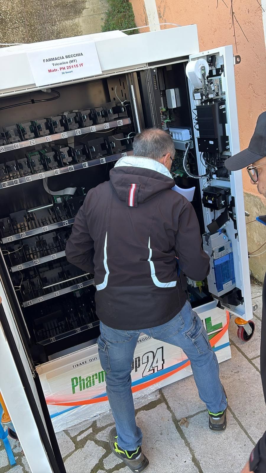 Un uomo in piedi davanti a un distributore automatico aperto, ne ispeziona l'interno e il cablaggio.