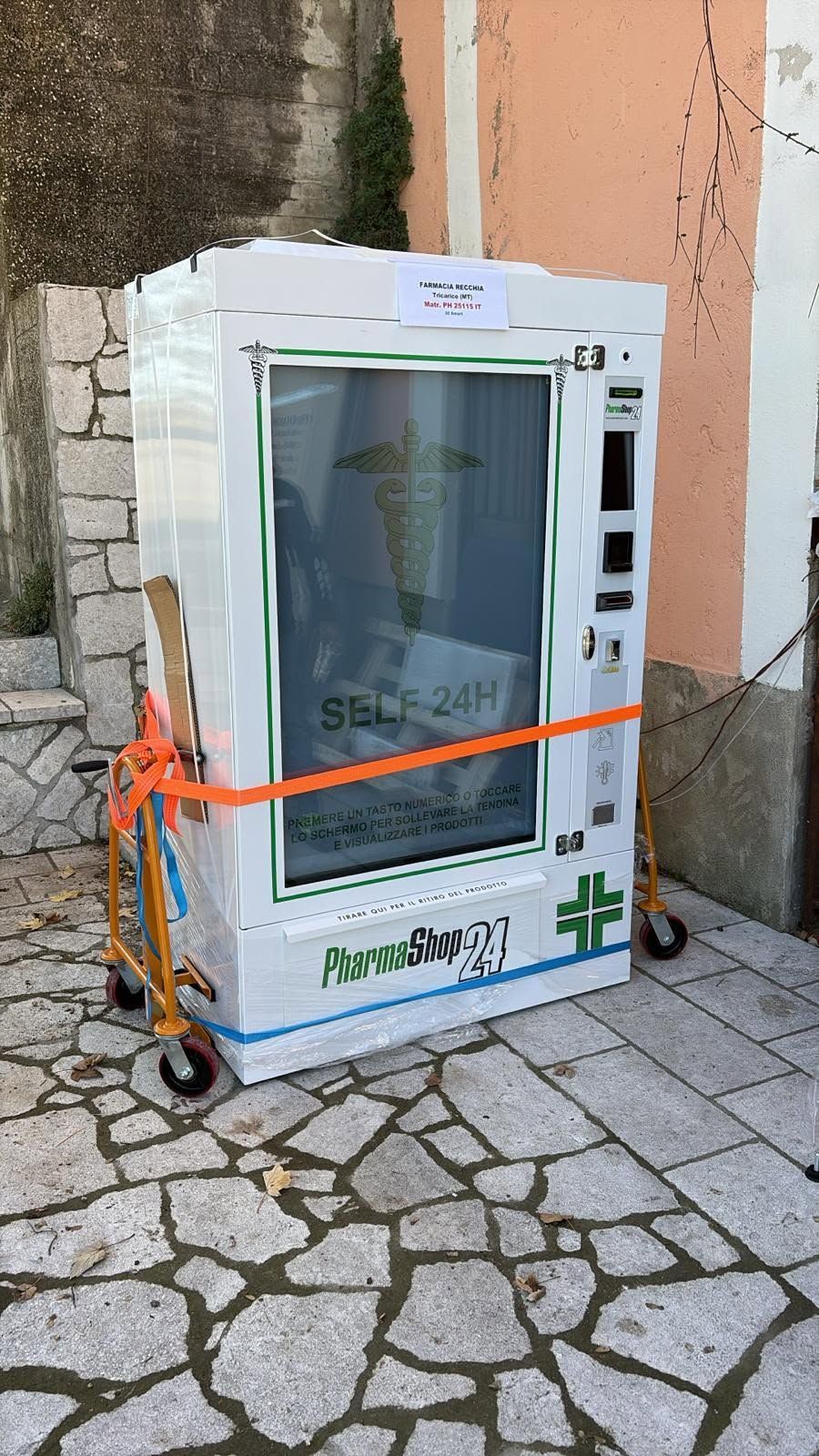 Macchina bianca fissata a un carrello a mano su un marciapiede di pietra accanto a un muro.