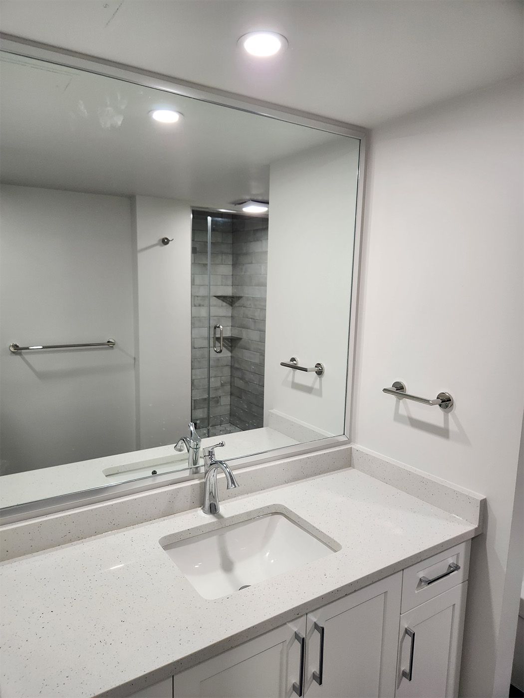 Bright modern bathroom vanity with large mirror, white countertop, and chrome faucet and towel bars.