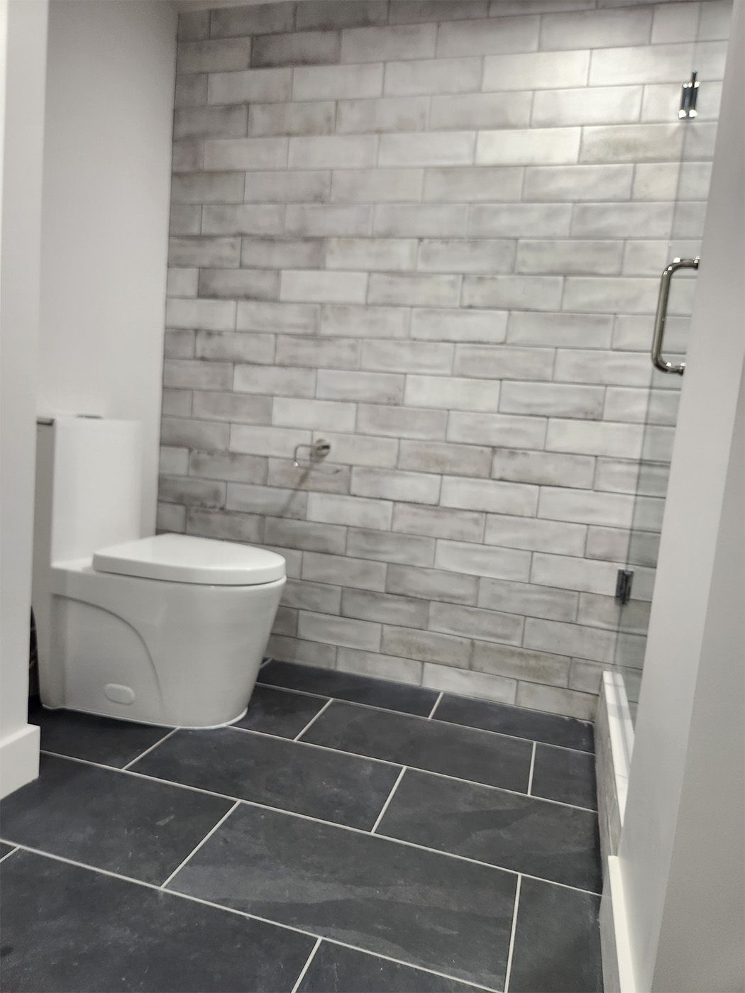 Accessible bathroom with white toilet, gray tiled walls and floor, and a grab bar in the shower area
