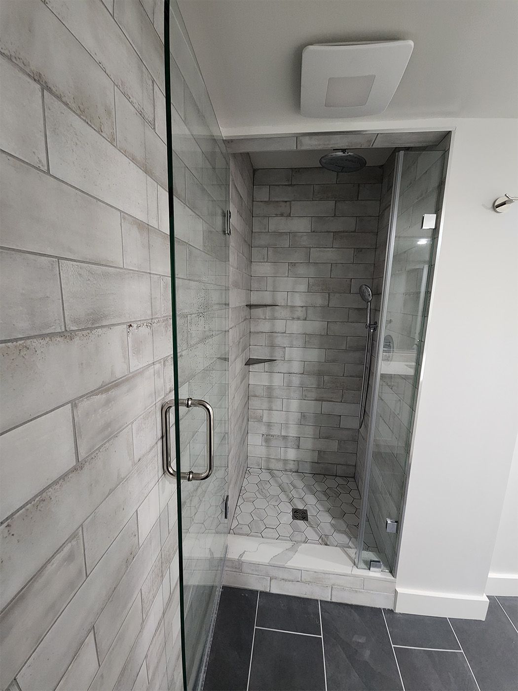 Gray tiled shower stall with glass door and white ceiling-mounted fixture in a modern bathroom