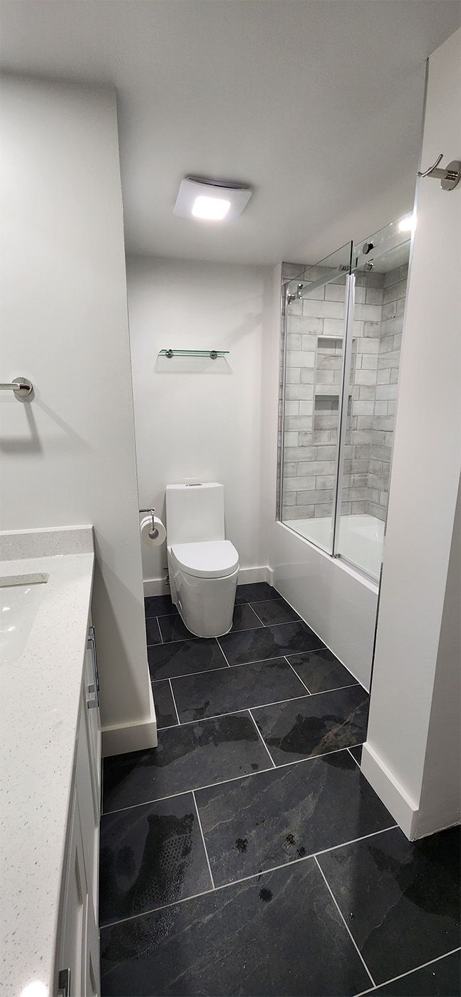Small tiled bathroom with toilet, sink, and bathtub, black floor tiles, white walls and ceiling light