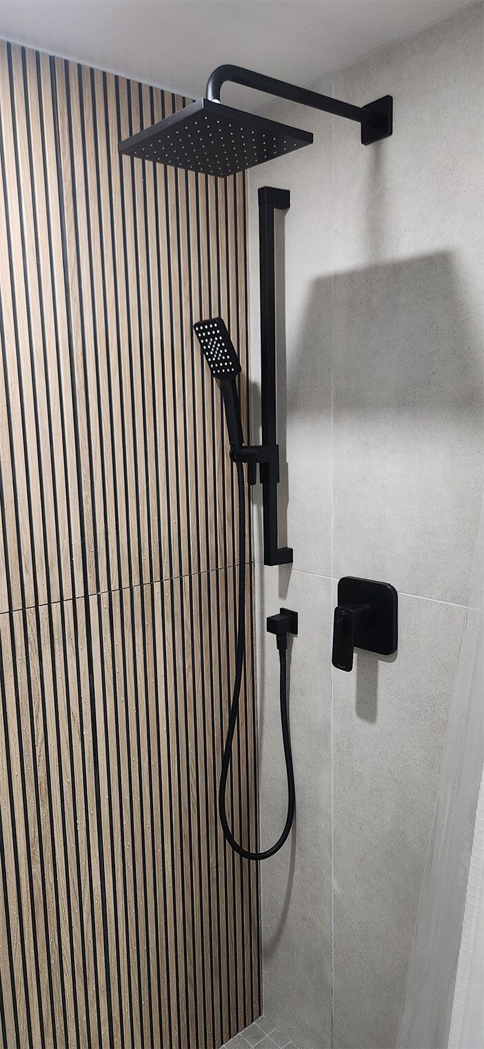 Black shower fixture with handheld sprayer in a tiled bathroom shower stall.