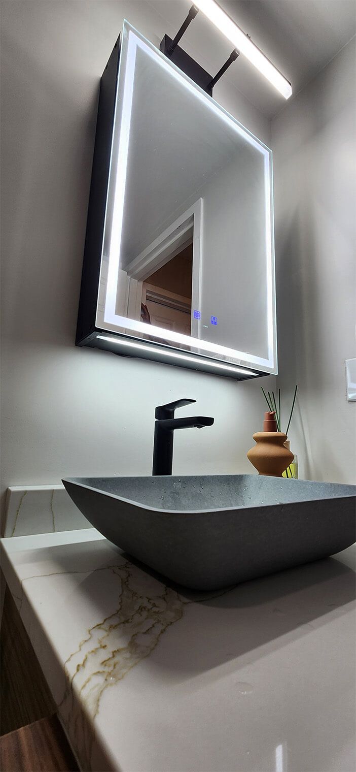 Modern bathroom vanity with lit mirror, black faucet, and round gray sink.