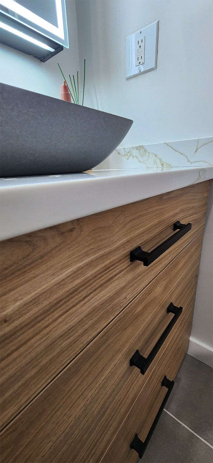 Wood-grain bathroom vanity with white countertop, black handles, and a sink
