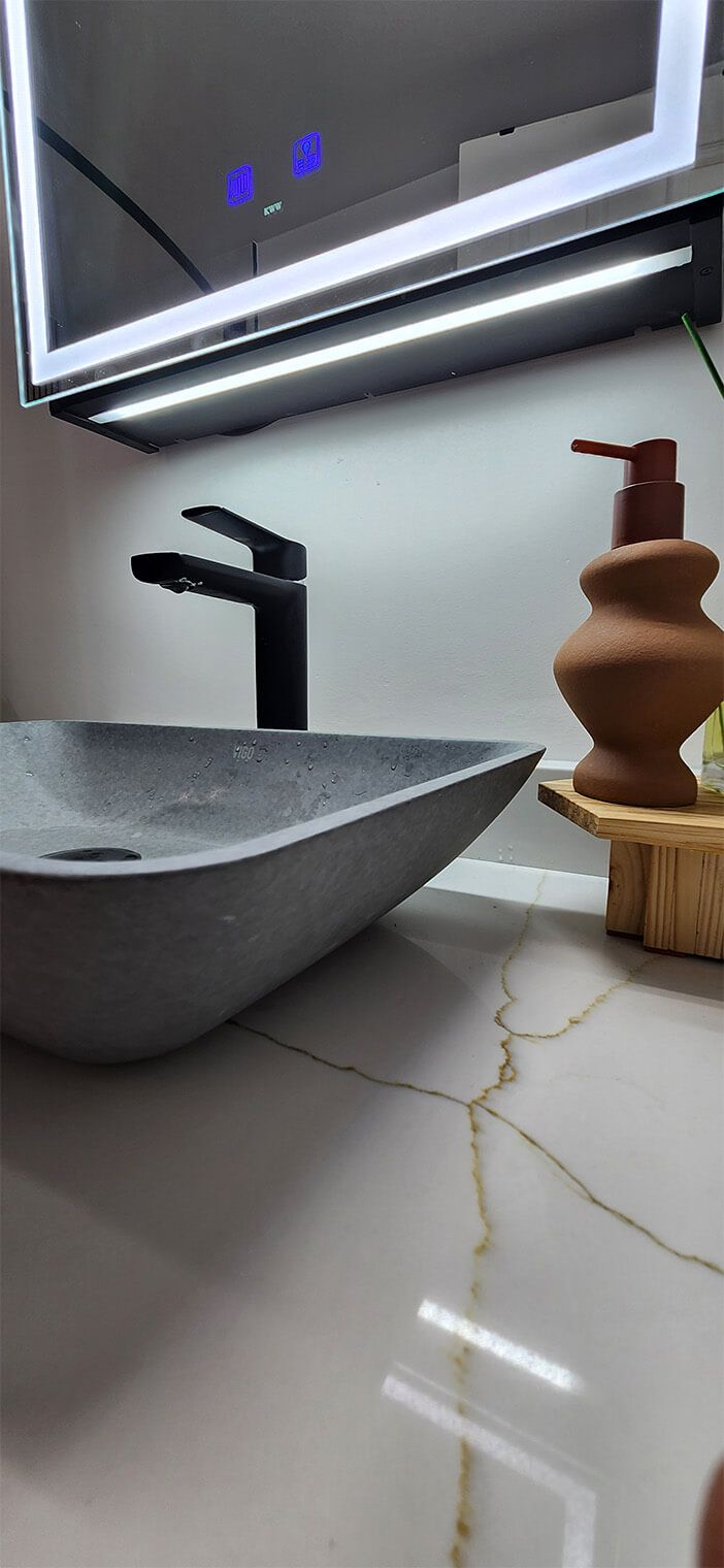 Modern bathroom sink with black faucet, decorative vase, and mirror lighting over white tiled counter