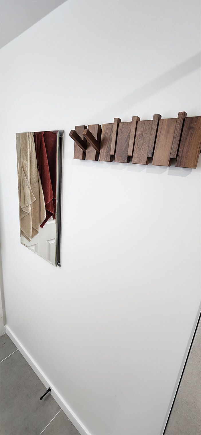Broken wooden wall art hanging on a white wall, with a detached piece leaning beside it