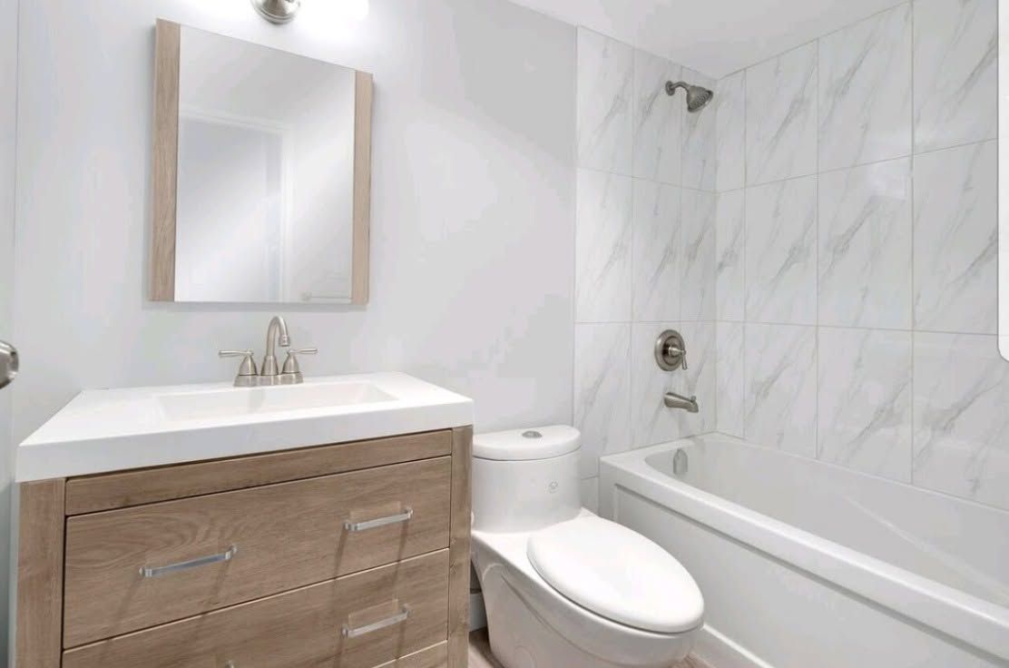 Bright white bathroom with vanity, mirror, toilet, and bathtub with tiled shower walls