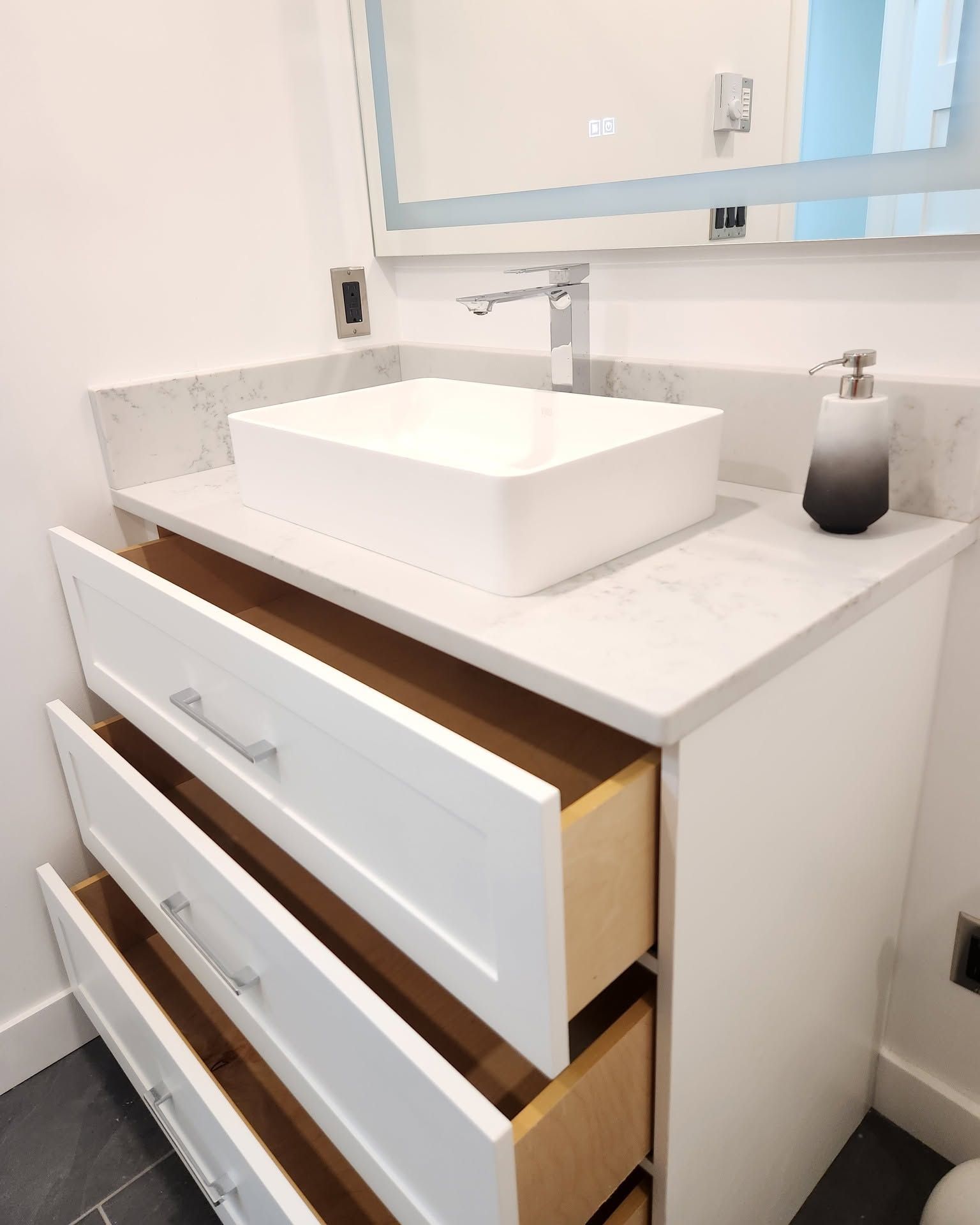 Modern bathroom vanity with white vessel sink, large mirror, and two open drawers revealing wood interior