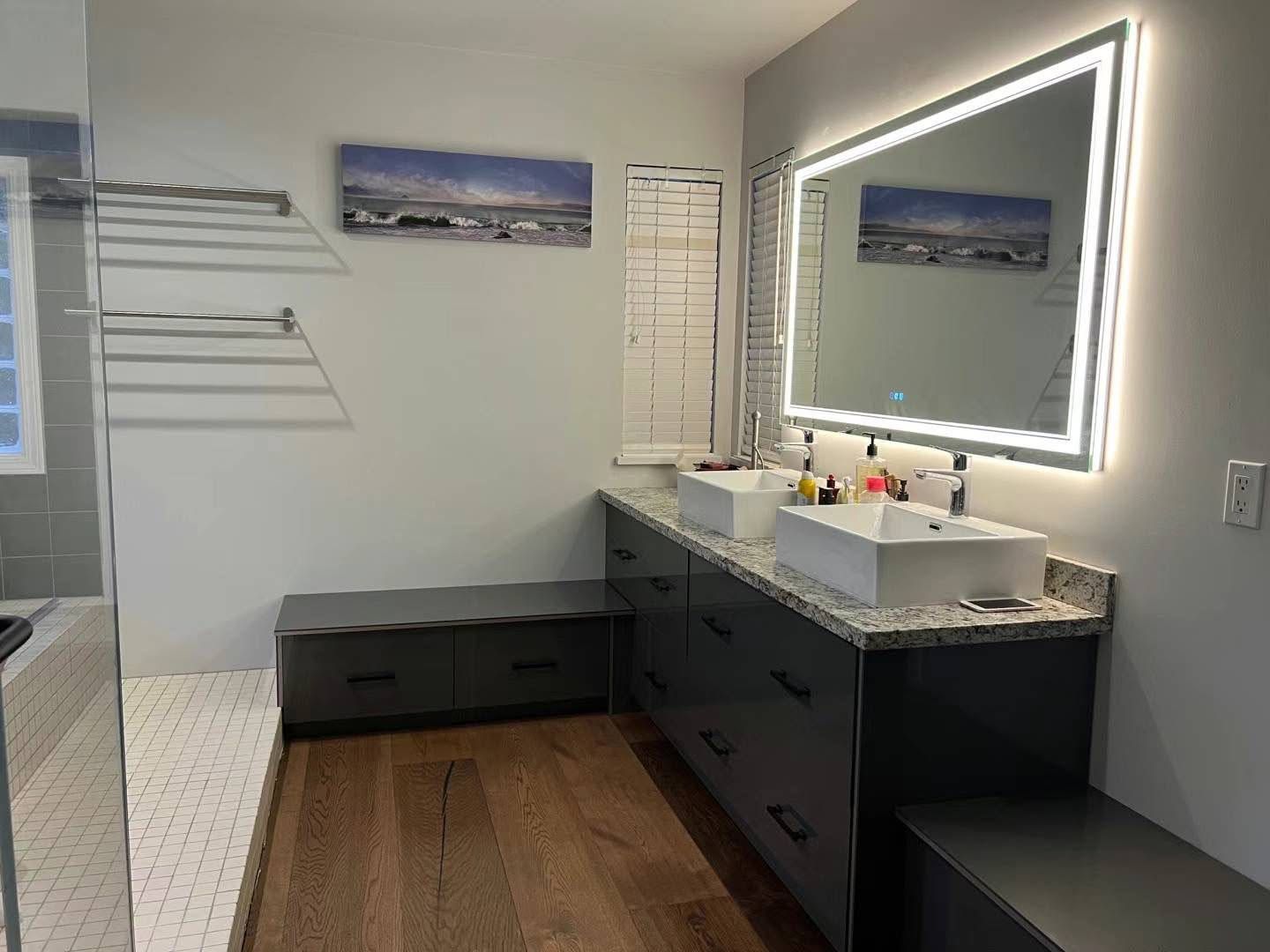 Modern bathroom with double vanity, lit mirror, gray cabinetry, and wood-look floor