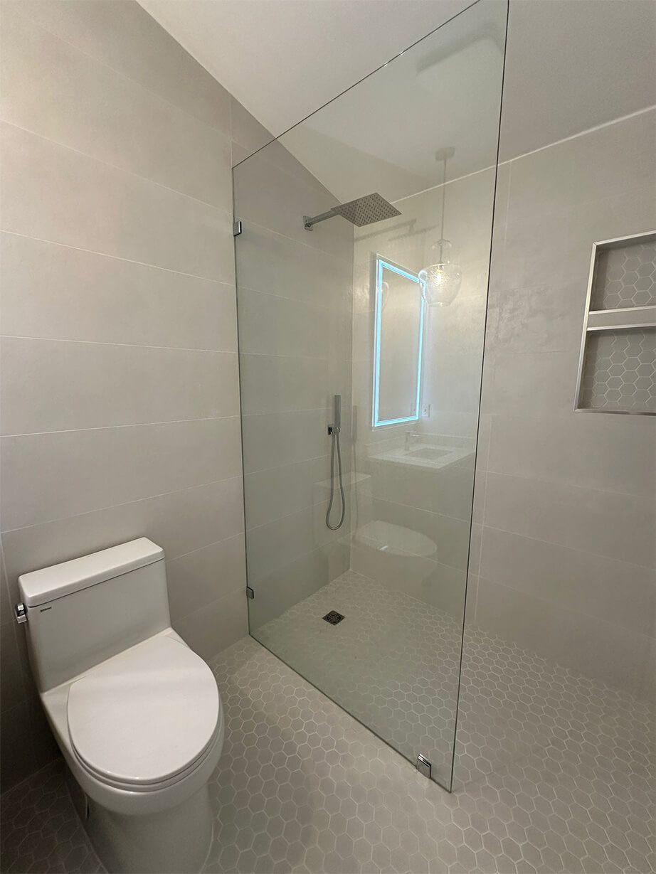 Compact white bathroom with toilet and large glass shower enclosure, bright tiled walls.