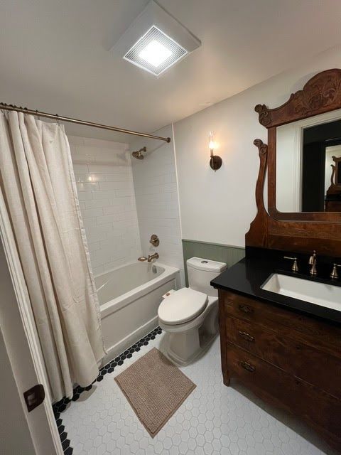 Small bathroom with bathtub, toilet, dark wood vanity, and large mirror under a skylight.