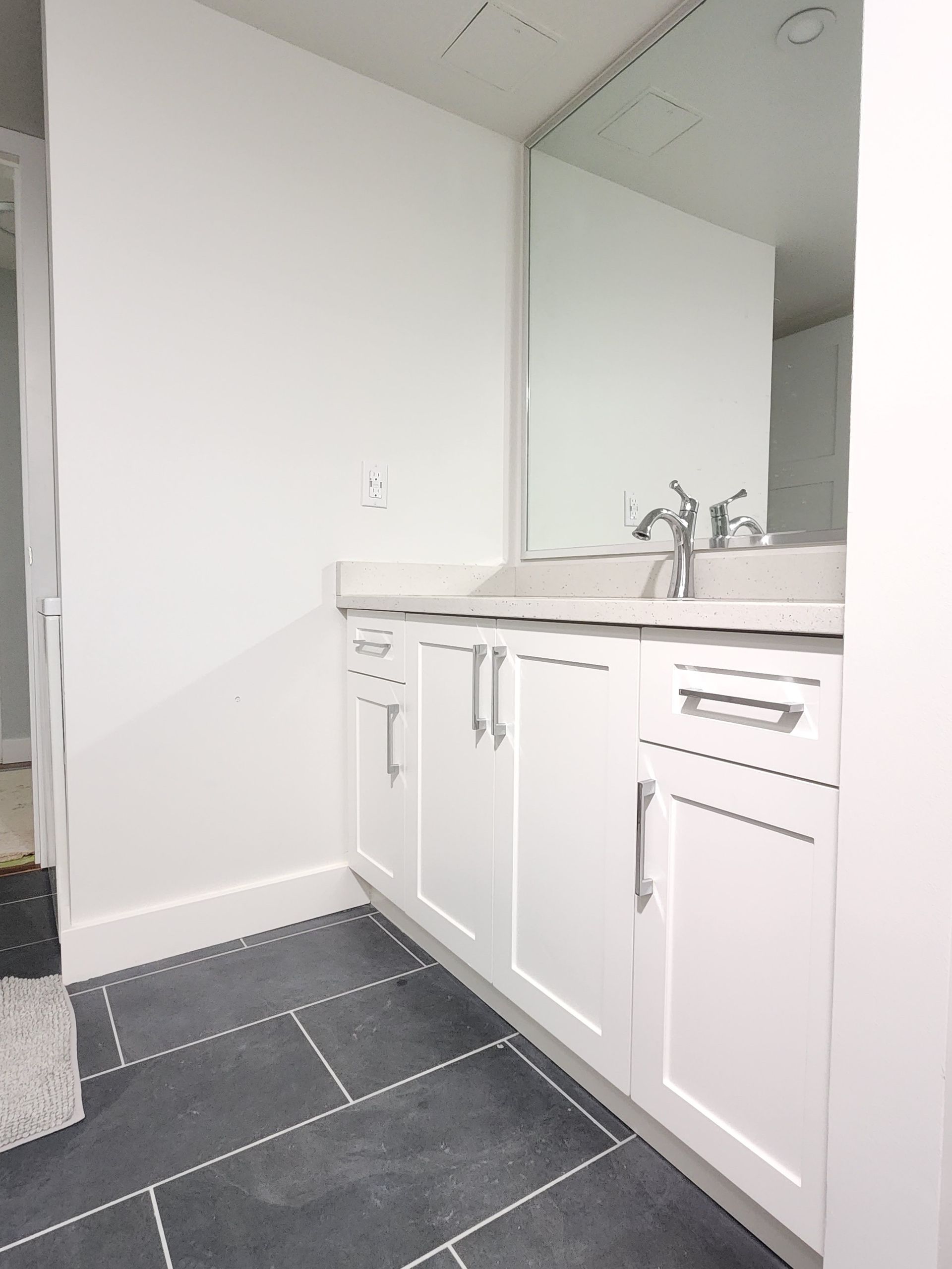 Small bathroom vanity with white cabinets, sink, mirror, and dark tiled floor