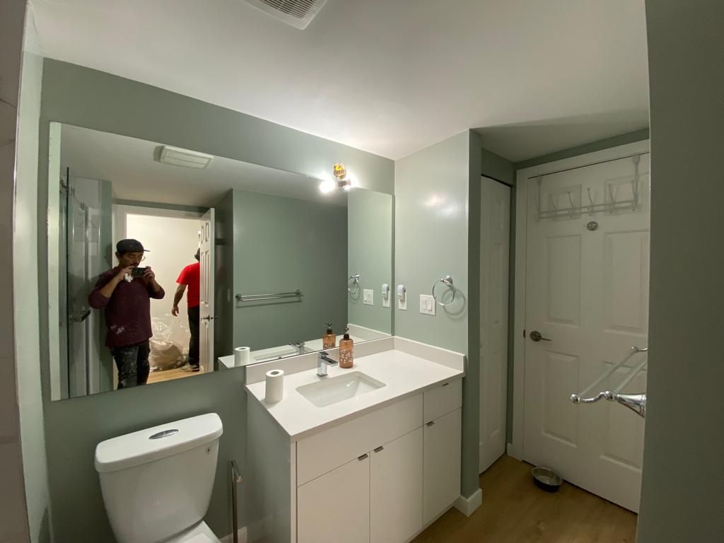 Bathroom with large mirror, white vanity, toilet, and a person reflected taking a mirror selfie.
