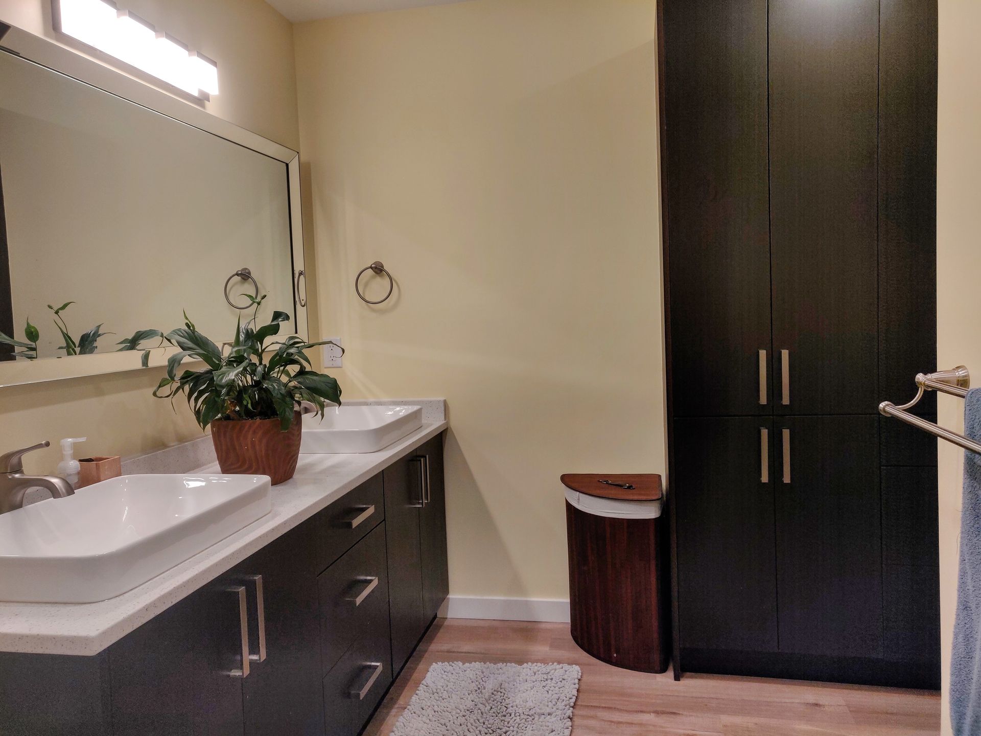 Modern bathroom with double vanity, large mirror, dark cabinets, and tall wardrobe cabinet