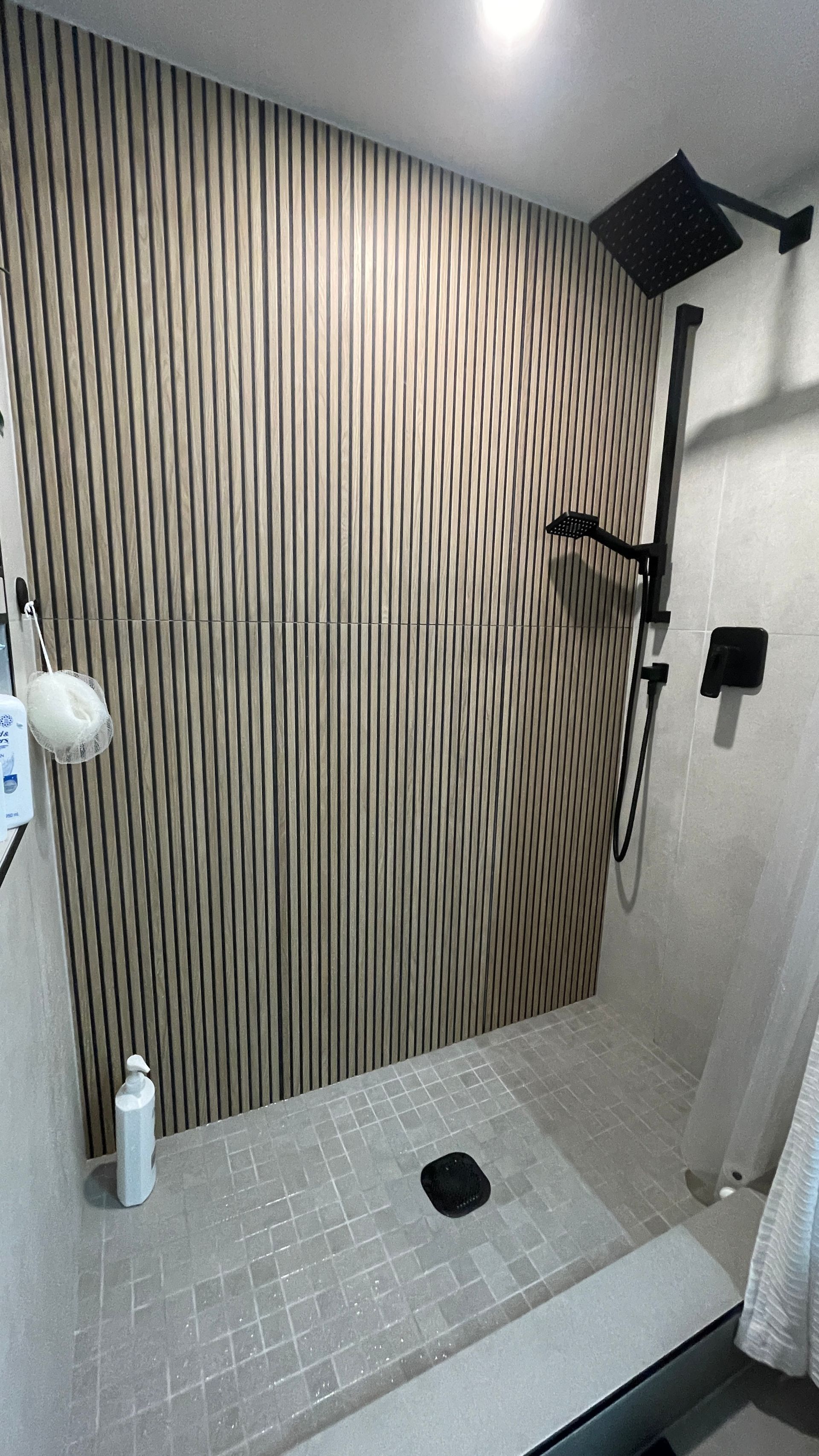 Bathroom shower with striped accent wall, tiled floor, handheld showerhead, and drain.