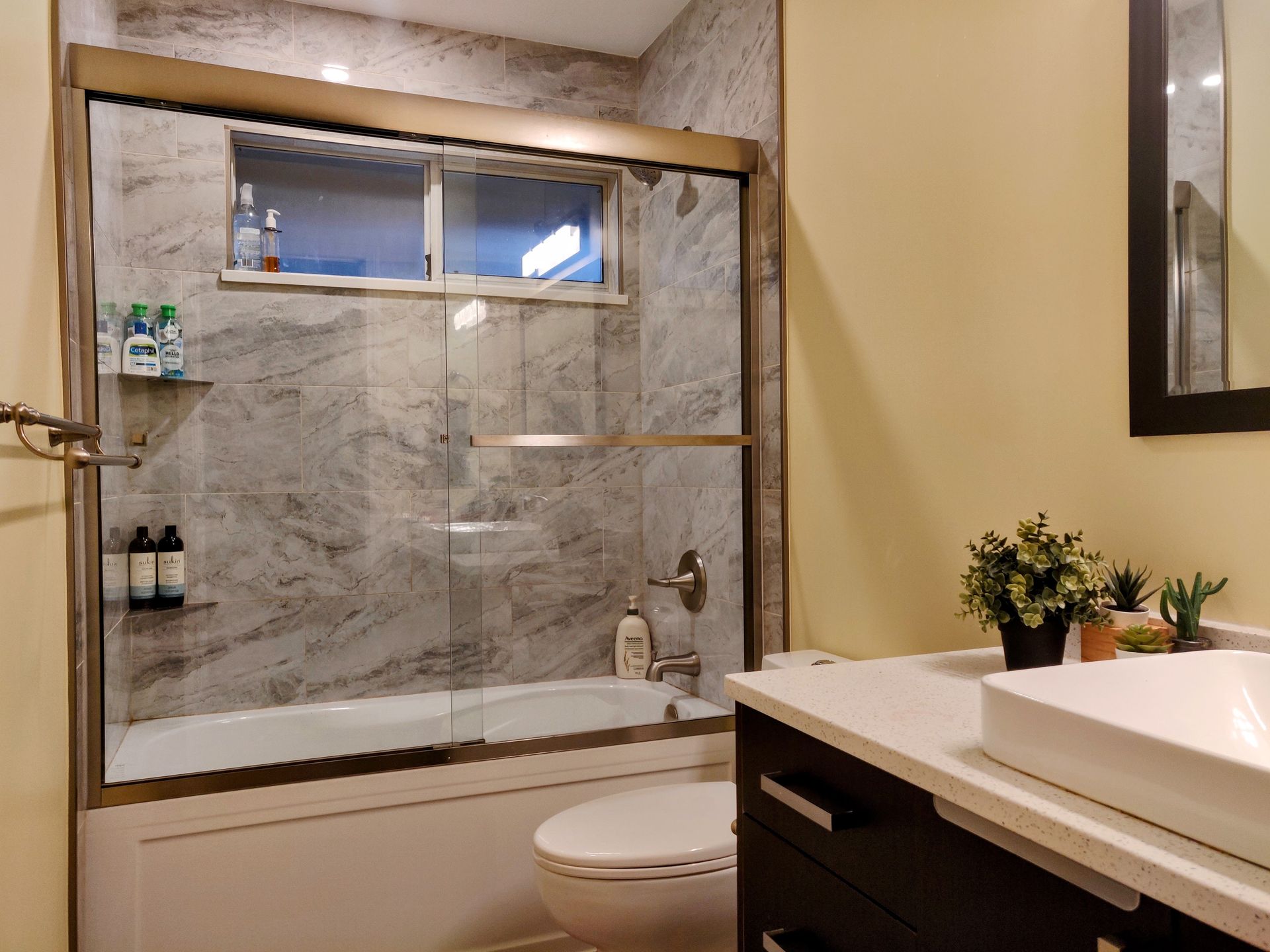 Bathroom with a marble-tiled shower, toilet, and sink vanity with a beige wall and mirror.