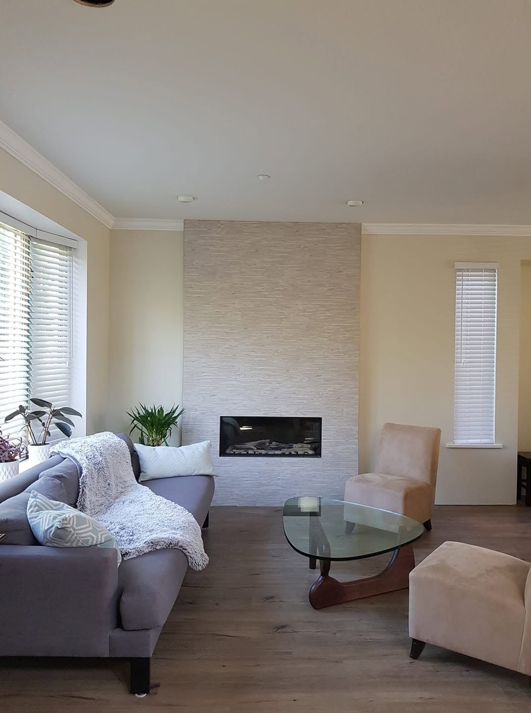 Bright living room with gray sofa, glass coffee table, beige chairs, and a fireplace.