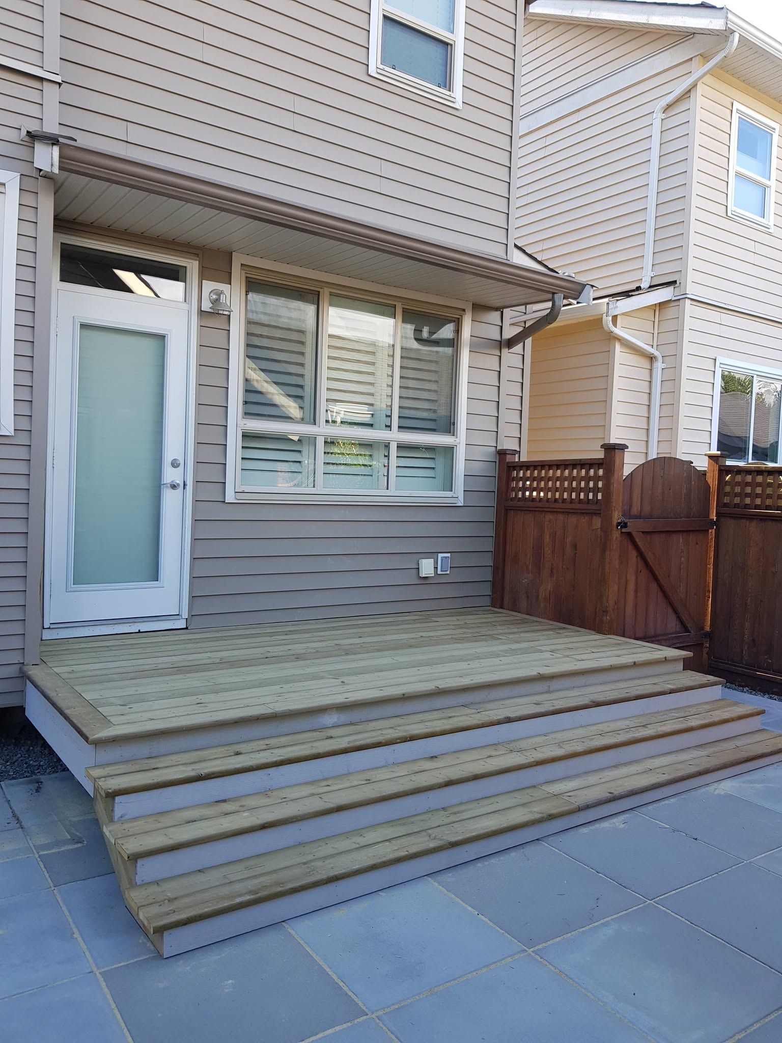Back deck and wide steps leading to a house entrance with beige siding and windows