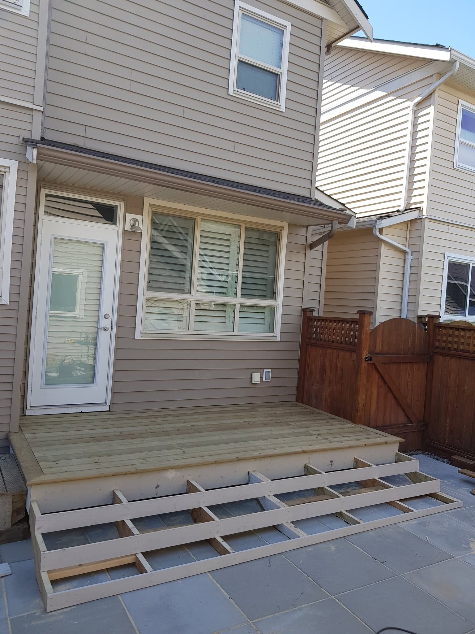 Backyard house deck with steps and a wooden fence, viewed from the patio
